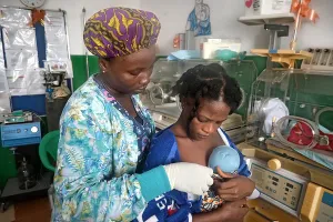 Woman holding newborn baby with nurse helping hold the baby