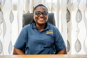 A woman wearing a blue shirt sits in an office chair smiling at the camera