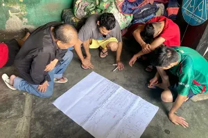 Four Mexican men gathered kneeling on the floor and gathered around a sheet of paper.