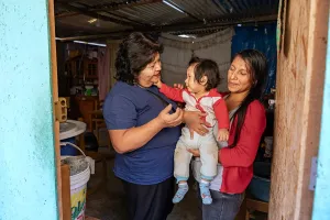 An older and younger woman stand in a doorway holding a toddler.