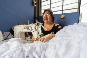 A woman sewing a pile of white fabric with a sewing machine in a blue room.