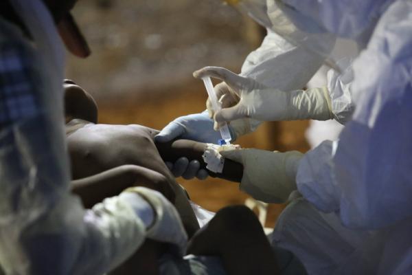 Medication being administered to a child through IV by medical workers wearing protective gear.