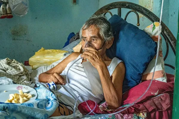 Leoncio Carrión rests in bed, wearing an oxygen mask.