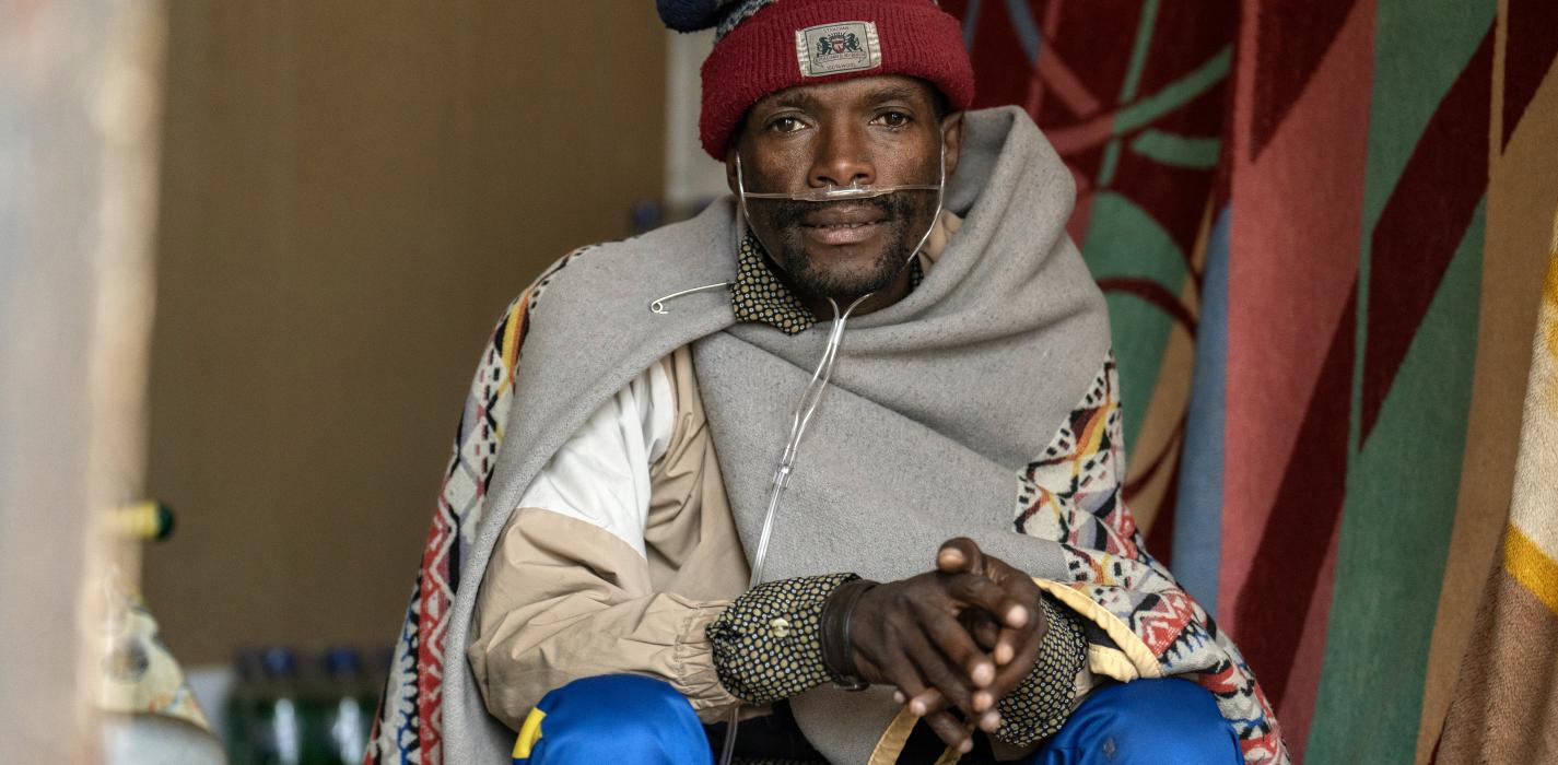 Portrait of Kaizer Mahapa wrapped in a grey blanket.