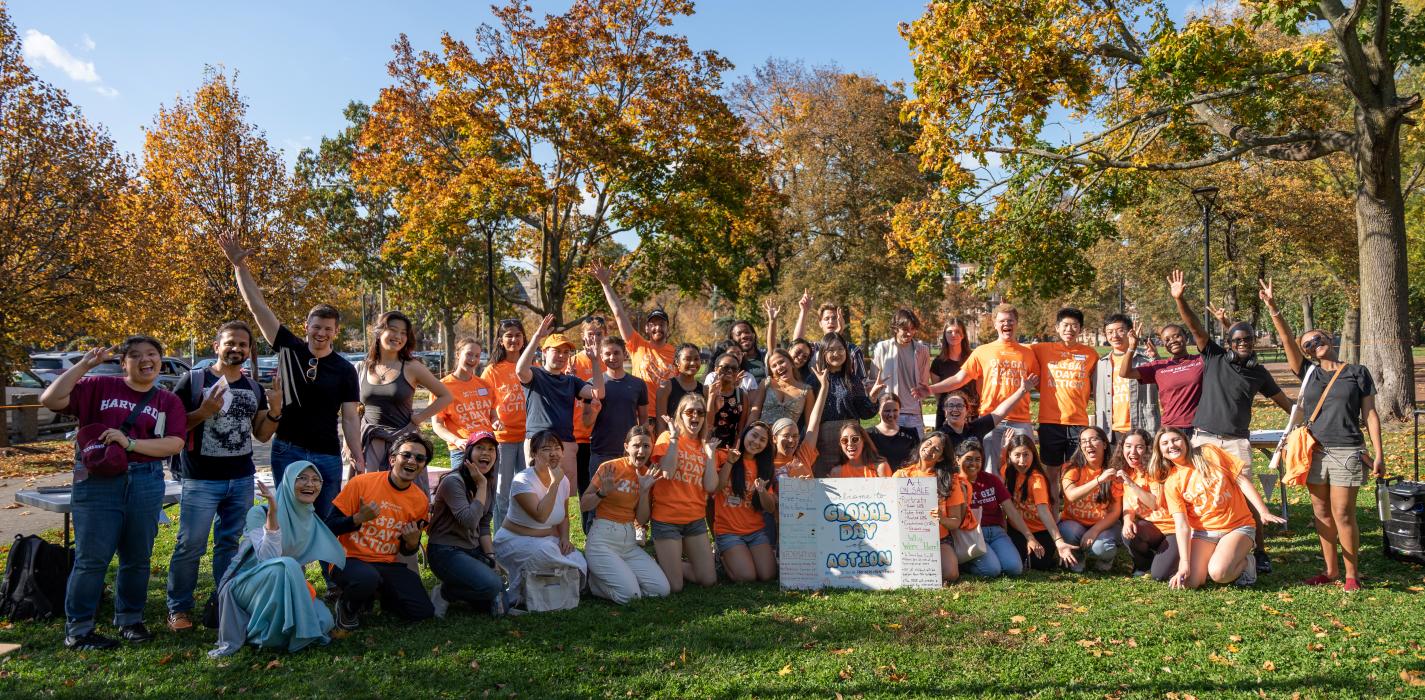 Students wearing orange t-shirts are gathered outside. They are posing in front of greenery.