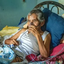 Leoncio Carrión rests in bed, wearing an oxygen mask.
