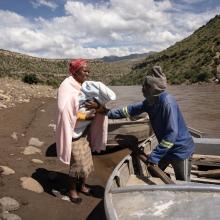 A new mom ‘Masebabatso Mokatlela from Ha Ramokatlela is being assisted to cross the river using a boat after a baby was born the day before.