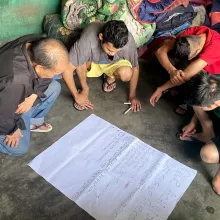 Four Mexican men gathered kneeling on the floor and gathered around a sheet of paper.