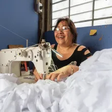 A woman sewing a pile of white fabric with a sewing machine in a blue room.