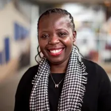 Basimenye Nhlema smiles at the camera in a black shirt with a black and white scarf