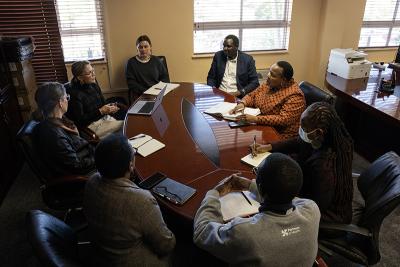 Staff sit around a conference table in a meeting, discussing and taking notes.