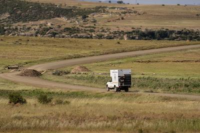 A white truck driving down a winding road surrounded by green grass.