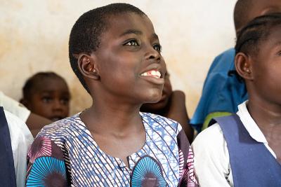 Dennis, smiling, looks up while seated with classmates in a classroom in Liberia.
