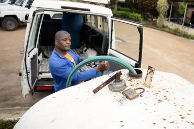 A man in a blue shirt holding a green hose in a large white fuel drum.