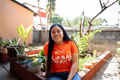 Woman sitting in front of rooftop garden, wearing orange t shirt. 