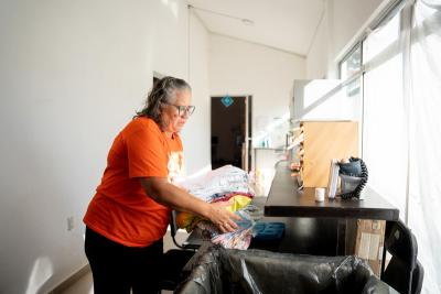 Woman in orange shirt gathering folded pieces of clothing to a basket