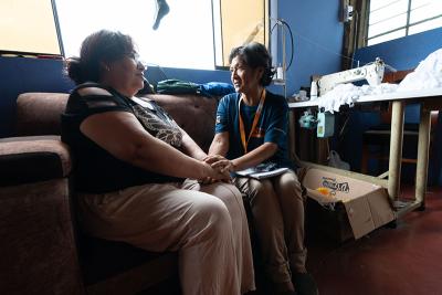 Two women sitting on a brown couch. One holds the others hands giving comfort.