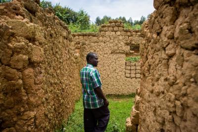 Olivier Kayitsinga walks through the unfinished stone house he is building, with grass underfoot.
