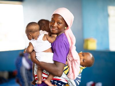 Kumba Comba carries her baby and the children of other mothers who are preparing Bennimix.