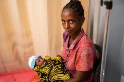 Mother holding her newborn wrapped in colorful cloth in a postnatal care room.