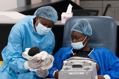Healthcare worker supporting a newborn during a post‑delivery check in a medical ward.
