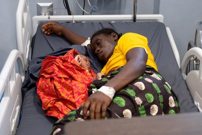 A mom sleeps next to her newborn in a hospital bed.