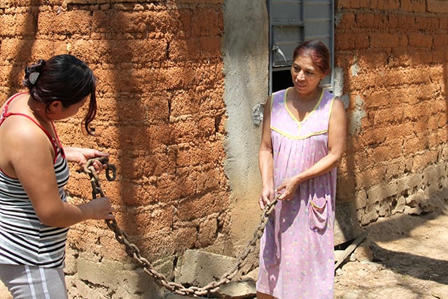 Velasquez (left) and Mirian Lopez stand in front of the shack where Rosemberg lived for six years and hold up the chain that used to restrain him.