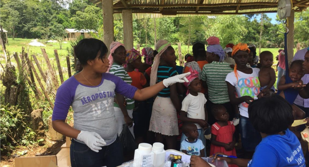 A PIH staff member distributes jars of Nourimanba and other medicine at a mobile nutrition clinic
