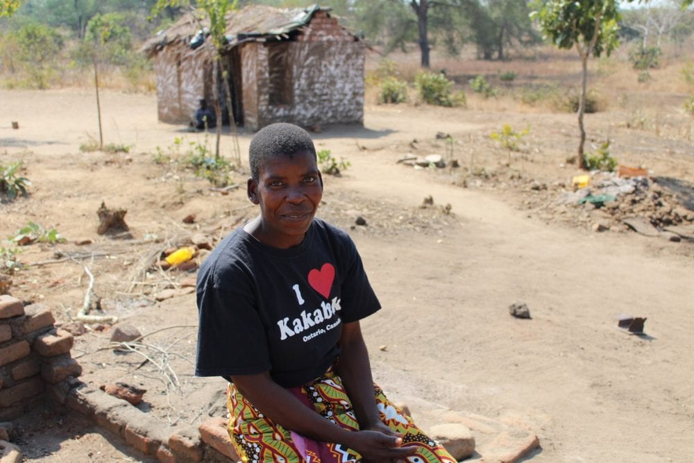 Idah sits smiling with a small house in the background.