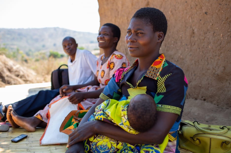 Agnes Paulo sits with her 6-weeks-old son Ulemu outside their home. Two PIH community health workers sit beside her.