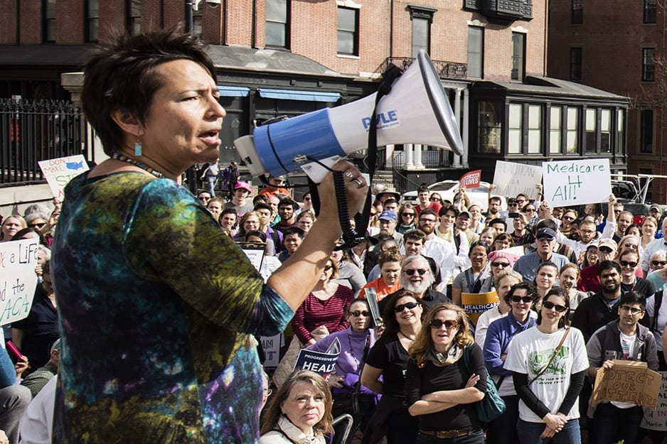 Dr. Joia Mukherjee stands in front of a crowd speaking into a megaphone
