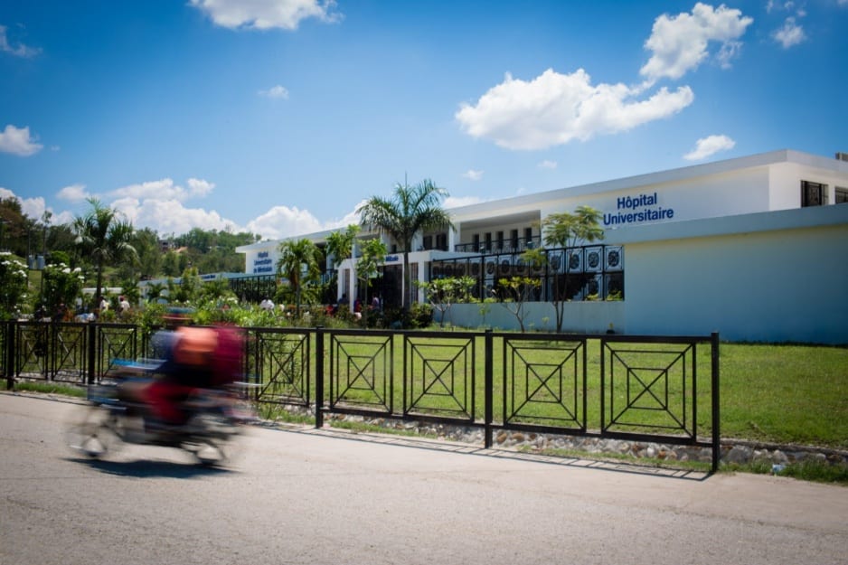 A motor bike drives past the front of University Hospital in Mirebalais