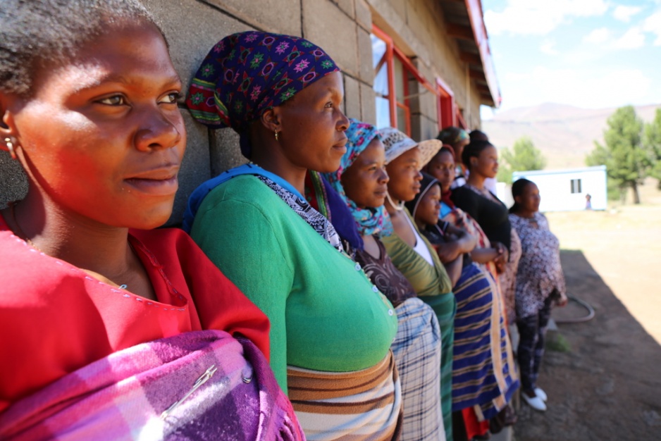 A line of women stand along the outside wall of a clinic
