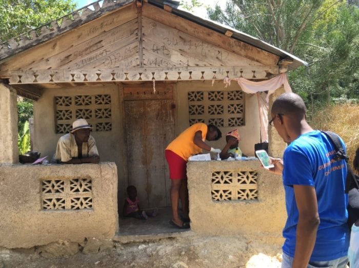 A PIH nurse and social worker visit a family outside the front door of their home