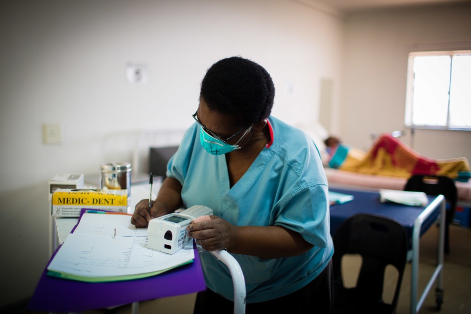 Nurse Mahali Lethetsa records patients' information with a TB patient in the background in bed
