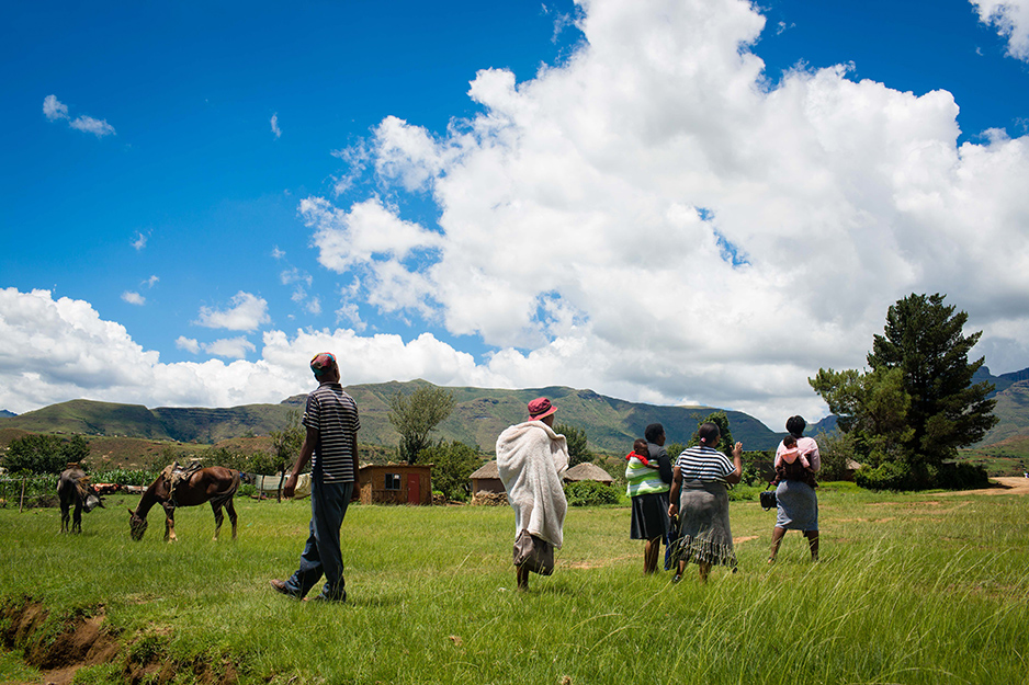 A village health worker walks through a field with three new mothers