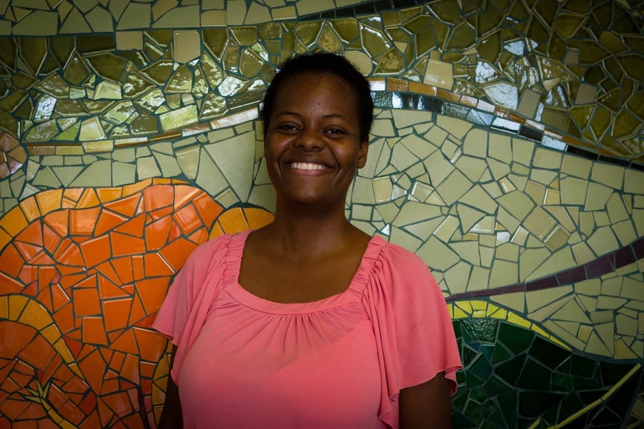 Oldine Deshommes stands smiling in front of a mural