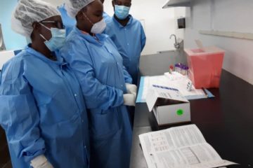 A group of staff in personal protective gear conduct a training on how to use COVID-19 rapid diagnostic tests.
