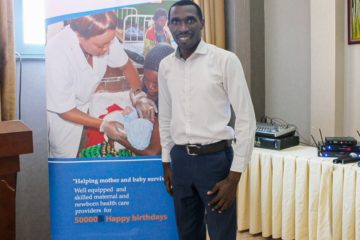 Nurse Andre Ndayambaje stands in front of a banner on maternal and child health